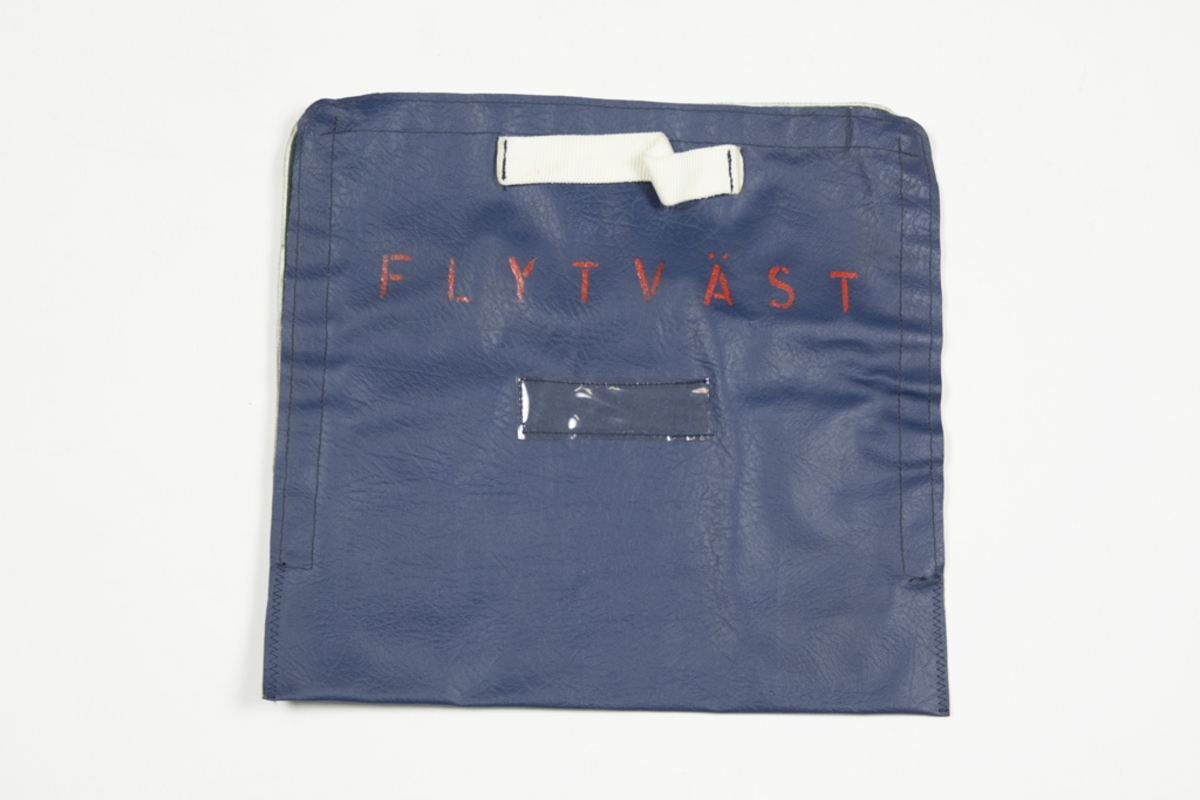 Blå packväska för flytväst i kabin på transportflygplan väskan fästes ihop med kardborreband runt tre sidor, handtag i vit nylon, på framsidan står det skrivet "Flytväst" i rött. Väskan fästes med två kardborreband.