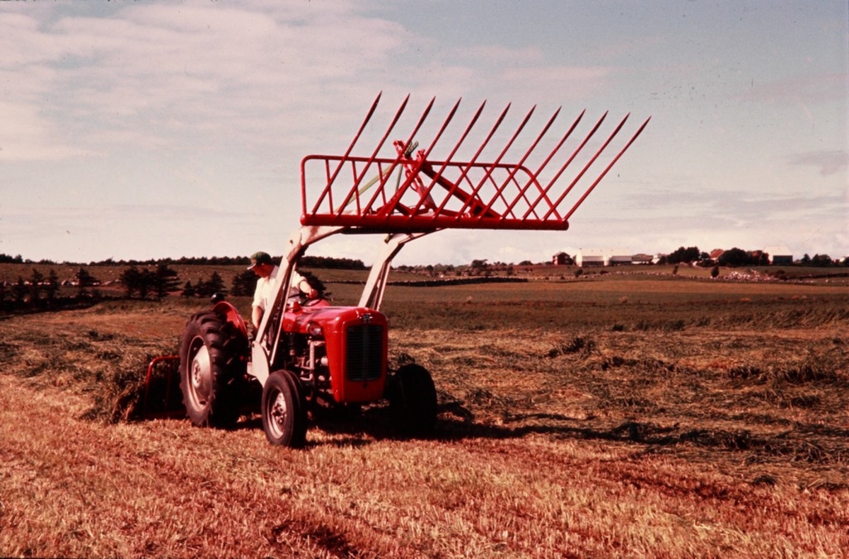 Lasting av gras med Silosvans fra Kvernelands Fabrikk AS, bak- og frontmontert på traktor, bilde tatt foran, sjåføren het Fimland