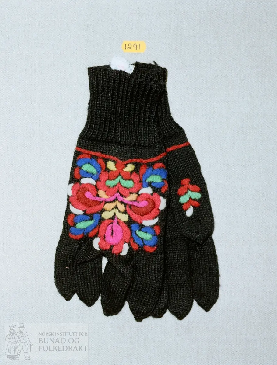 1 par fingervanter i glattstrikket svart ull, med rosesøm på handbaken (Hallingrose) i sefyrgarn i flere farger.