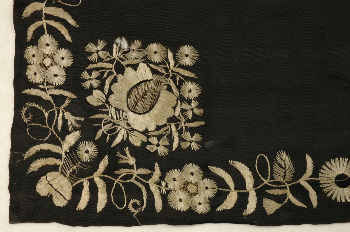 Kvadratisk tørkle i svart silke med påbroderte blomstermønster. To sider har fargerikt mønster, mens den andre har kvitt mønster.