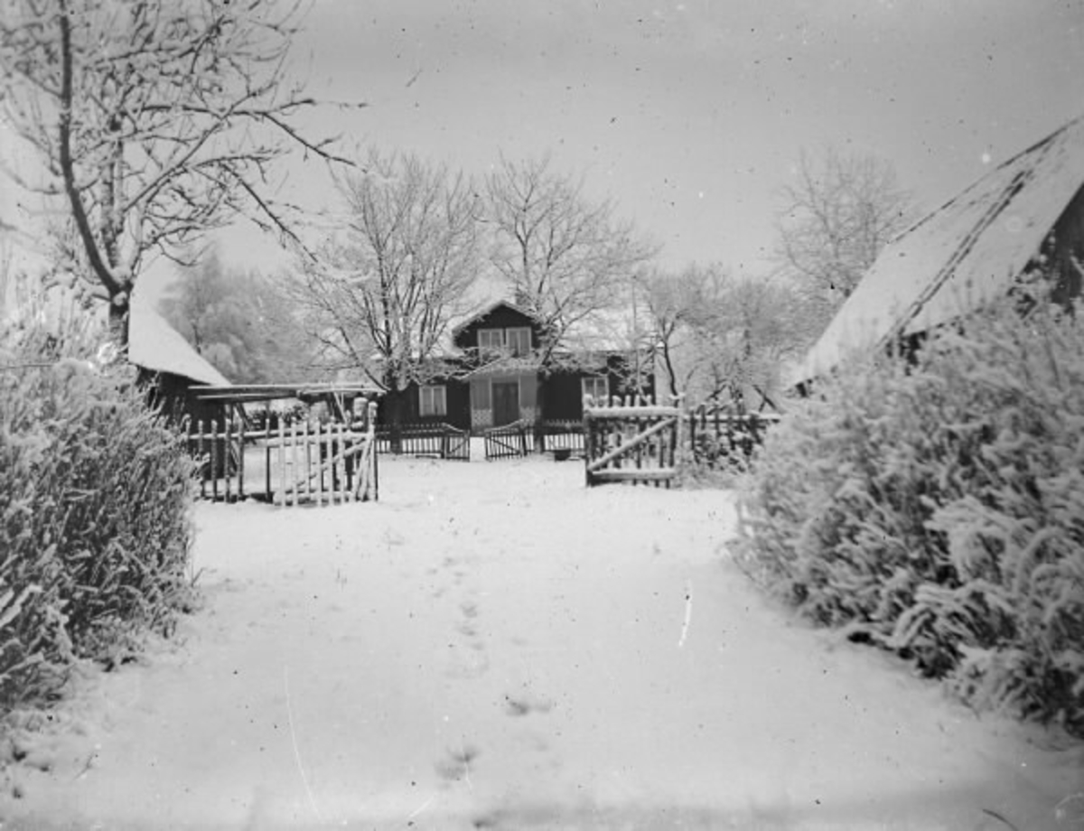 Gården Ugnhult 1:3 fotograferad i snöskkrud under 1920-talet. Uppfarten kantas av buskar. Vid sidorna ligger ekonomibyggnaderna och mangårdsbyggnaden ses rakt fram, omgiven av träd. Tomten avdelas genom två trästaket med dubbla grindar.