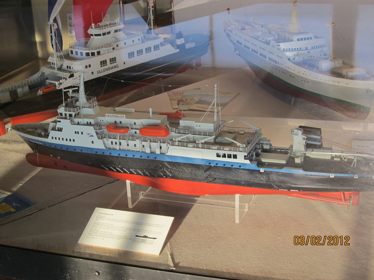 Modell av hurtigruteskip ,1:100, lastedekk akterut på modellen (senere ombygget). Rødt uv-skrog, sort fribord med blå stripe øverst, hvitt overbygg. Modellen viser skipet før rederiet ble overtatt av Ofoten.
