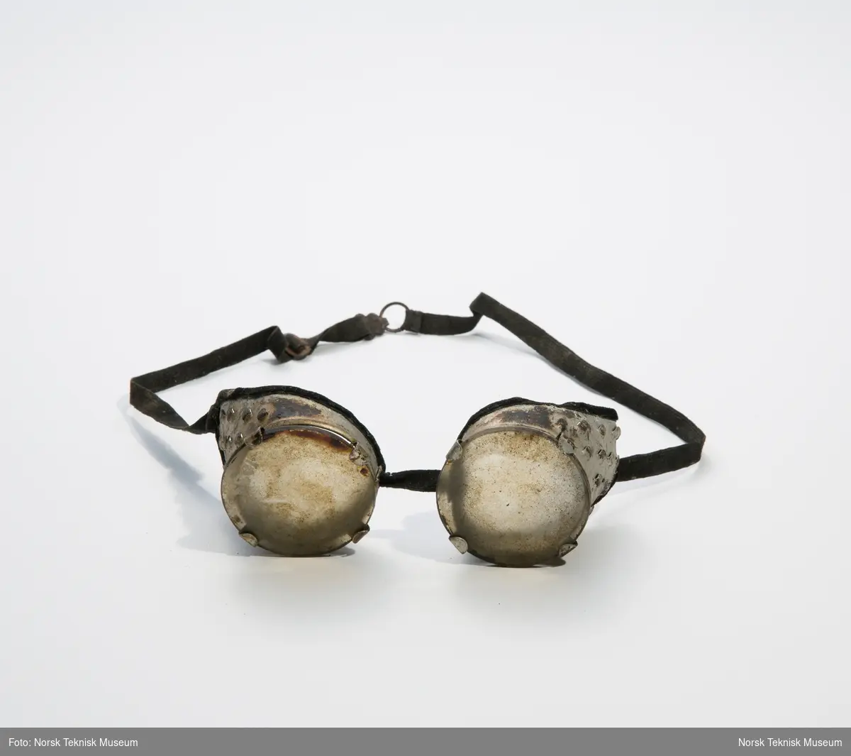 Beskyttelsesbrille med innfatning i aluminium og runde glass i glass. Med strikk til hodet.