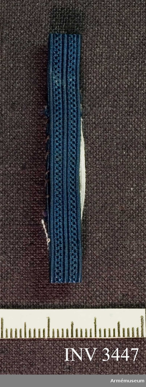 Längd: 100 mm.Blått band, 7 mm, för vice tjänstegrenschef eller detaljgruppchef SLK. Att fästas runt axelklaffens bas. Ett  blått mönstervävt sidenband. Bäres ett på vardera axeln.