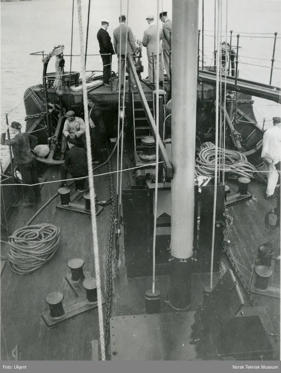 Fire menn studerer hvalkanonen på dekk på hvalfangstskipet D/S Hektor II (senere omdøpt til Norman I), B/N 458 under prøvetur i Oslofjorden. Arbeidere sitter rundt på dekk. Skipet ble levert av Akers Mek. Verksted i 1930 til A/S Hektor, ved skipsreder N. Bugge, Tønsberg.