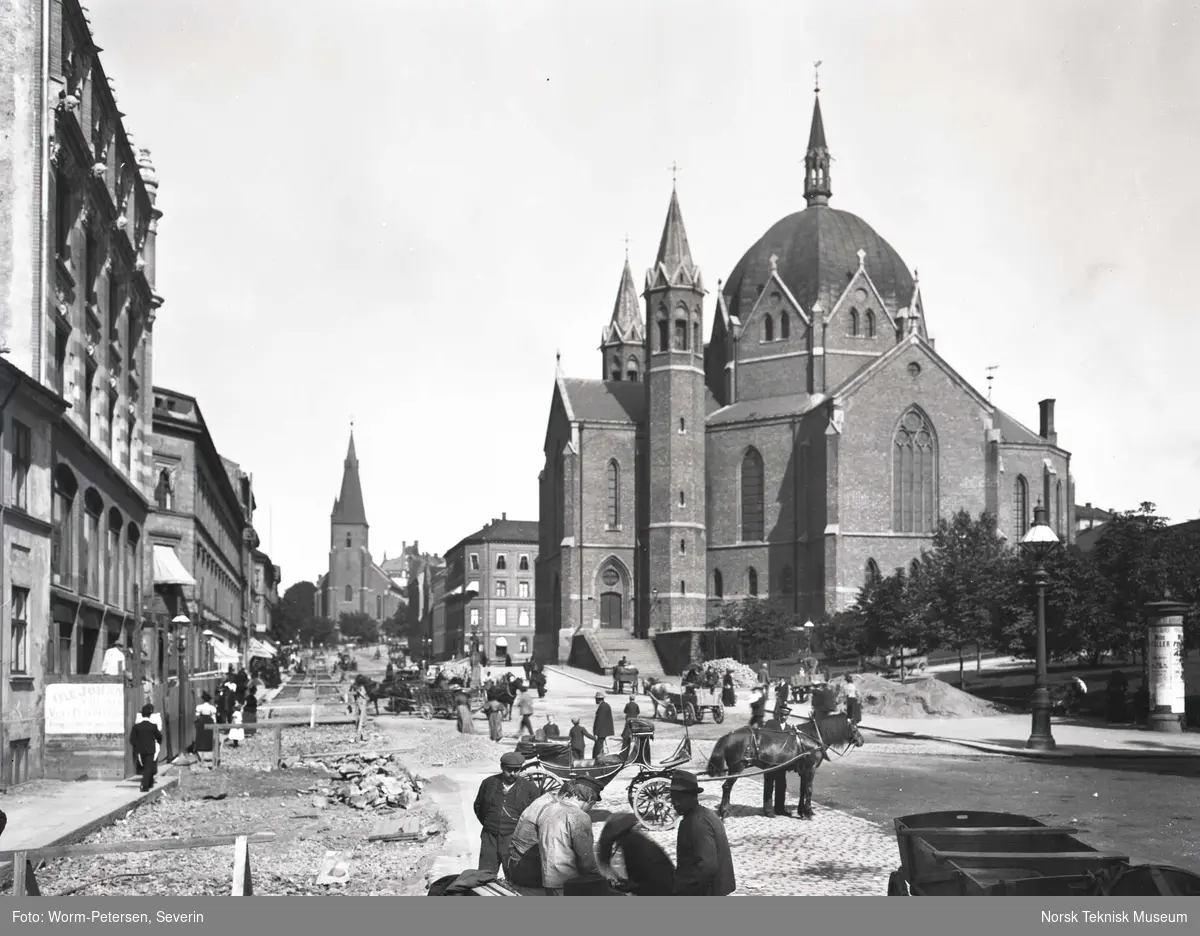 Legging av trikkeskinner i Akersgata i 1899. Bildet er tatt under arbeidet med ny sporvei fra Akersgata 18 der leseselskapet Athenæum lå, til St.Hanshaugen. Trefoldighetskirken ligger til høyre og St.Olavs kirke i bakgrunnen.