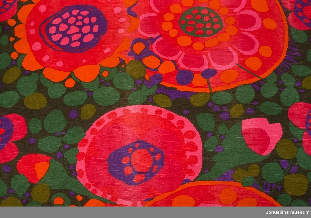 Funktion: Rumsavskiljare i tångbadhus.
Draperi av bomull, tryckt blommigt mönster i grönt, rött, rosa och lila på ripsartat (inslaget)vävt tuskafttyg.
Ljusare slitna ränder, enstaka hål.
Mönstret heter "Ekerö", och ritades av Saini Salonen runt 1969 till kollektionen "Linje Hemma" för Borås Wäfveri.