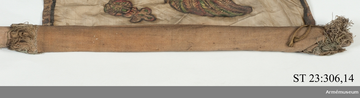 Duk av vit sidentaft och strumpa av rött linne försedd med frans vid öppningarna. Motivet målat i guld- och silver samt rött och grönt bestående av en krönt örn, måne, sol och stjärnor, På duken en pappersetikett som anger att den tagits i slaget vid Saladen 1703.