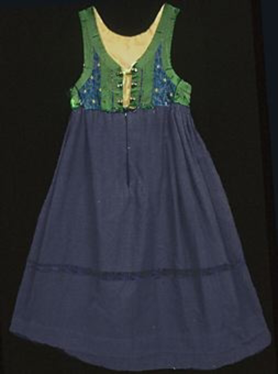 Livkjol med mönstrat, bandkantat liv och mörkblå kjol. Livstycket är sytt i mönstervävt tyg med blå bomullsvarp och rosa silkeinslag. Ytan är dekorerad med plattsömsbroderi i form av gula stiliserade blommor och gröna prickar, stygnen har sytts genom två tyglager; ett mellanliggande tyg i oblekt linne. Livet är kantat och dekorerat med ett grönt ca 35 mm brett ripsband. Bakstycket har två påsydda gröna band som bildar en svängd V-form, vecken har sytts ned med flätsöm i grönt. Livet är sytt av ett bakstycke och två framstycken, det är helfodrat med oblekt linneväv i tuskaft. Mitt fram, intill öppningen på vardera framstycke är tre silvermaljor fastsydda, en av dem är något större än de övriga. Öppningen fortsätter i ett 270 mm långt sprund på kjolen. Sprundet knäpps med en tryckknapp och en hyska och hake, ovanför haken sitter ytterligare en hake med en trådögla. Kjolen är sydd i blålila tuskaftad oberedd ylleväv av tre våder; en fram och två bak. Ett blått 30 mm brett mönstrat sammetsband är påsytt runt om på kjolen 300 mm ovanför fållen. Kjolvidden är samlad i små rynkor längs hela bakstycket. I sidorna har livet tagits in, tyget har vikts i ett veck som hålls ihop med en enkel söm, kjolens rynkor ligger i dubbla lager. Kjolfållen är skodd invändigt med en 110 mm bred remsa i blått bomullstyg, sprundet mitt fram är också fodrat med blått bomullstyg. Sidficka samt kantning av kjolens sömsmån upptill i rutigt blått bomullstyg. Kjolen har varit avkortad/uppvikt och fållad ytterligare en gång, fållen har nästan helt släppt. Liv längd: 390 mm. Kjol längd: 890 mm. Kjol vidd: 2680 mm. Kjolen är ihopsydd på maskin, övriga sömmar är handsydda.