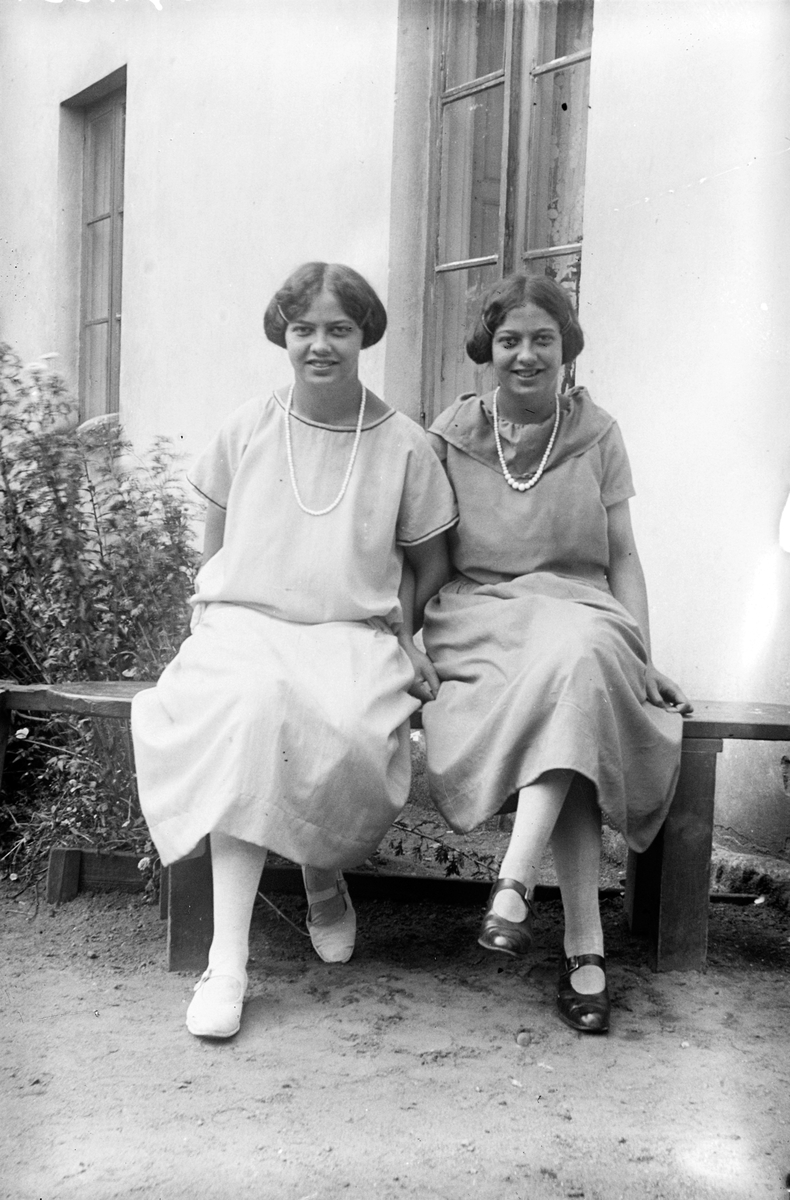 Två kvinnor sitter på en bänk framför ett hus.