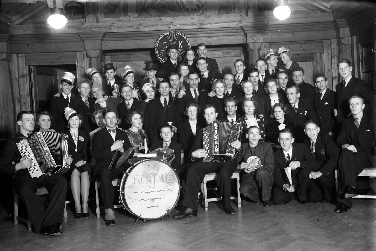 Gruppbild av Cykelklubben Revansche, år 1936. På väggen bakom dem hänger deras emblem, CKR.
Sittande i första raden: nr 3 från höger är Einar Andersson.
Stående i andra raden: Ordförande Nestor Lund (8).
Två män har dragspel i knät och en sitter vid trummor med texten ROYAL på.