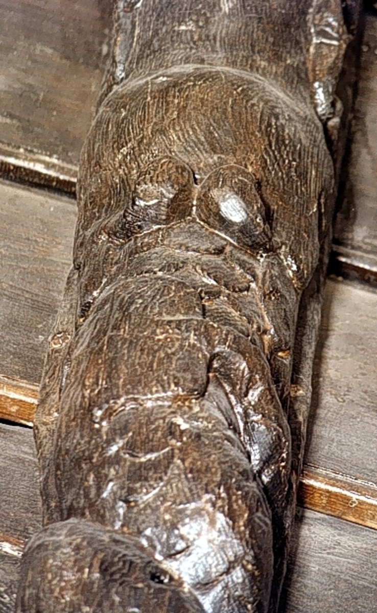 Nereid med uppåtkammad frisyr och hög, välvd panna. På huvudet sitter stora plymliknande bladflikar eller dylikt. Armarna är ersatta med dekorativa bladslingor som även markerar övergången till den fjällförsedda fiskstjärten. Fiskstjärten slingrar sig kring stjärten till en fisk eller en delfin, vars huvud är synligt vid skulpturens fotända.

Bakstycket är kraftigt och snidat i ett med skulpturen. Baksidan är försedd med hak eller urtag. Skulpturens profil är svagt S-formad.
Skulpturen är välbevarad.

Text in English: Nereid with hair combed upward and with high, arched forehead. Plume-like headgear. The arms are replaced by decorative rolled, leafy ornamentation which also marks the transition between the upper and the lower body. The fish tail is entwined with the tail of a fish or dolphin whose head can be seen at the foot of the sculpture.

The backboard is robust and carved in one piece with the figure. The back side of the backboard is carved with hollowed out grooves. The profile is slightly S-shaped.
The sculpture is well preserved.
