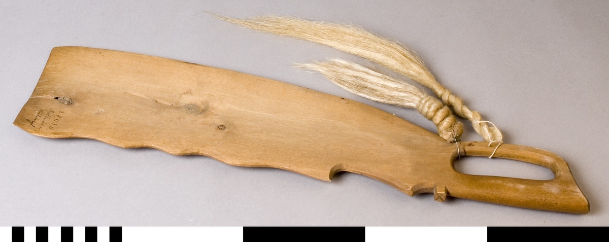 Handskaka av trä.  Formad som en kniv med blad och handtag. Bladet är profilerat. Handtaget med ögla och grepp.