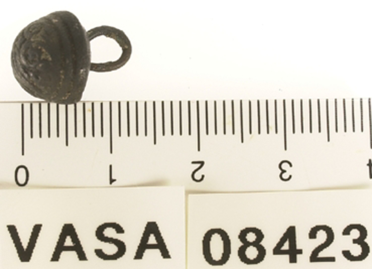 En rundad knapp med halvkonisk undersida och trådögla, samt dekor på huvudet.



Text in English: Two decorated metal buttons.

One is broken, and in an envelope in the magasin. This is a half-sphere shape with a rounded bottom edge.  The decoration is too abraded to be deciphered clearly. The shank has been broken off right at the head, evidence of wire shank still in holes in head.  Shank is in envelope with head.

Full button is located in livet ombord.  It is a half-sphere shape with a slightly convex bottom.  The decoration is too worn to decipher clearly, but it appears asymmetrical, with no centering motif on top.  The wire shank is cast in.