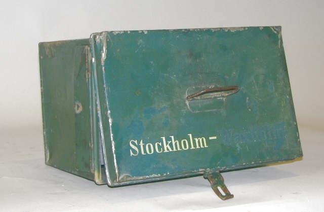 Brevlåda, grön med klaffförsett brevinkast på ena gaveln.
Öppningsbar genom en med hänglås låsbar taklucka. Brevlådan har ett
bärhandtag fäst på takluckan. Text i vitt på ena långsidan: "I
breflådan må icke nedläggas: bref som innehålla penningar, ej heller
försändelser under band." På takluckan text i vitt: "Stockholm -
Waxholm", där Waxholm syns mycket svagt. Troligen har man försökt ta
bort "Waxholm".