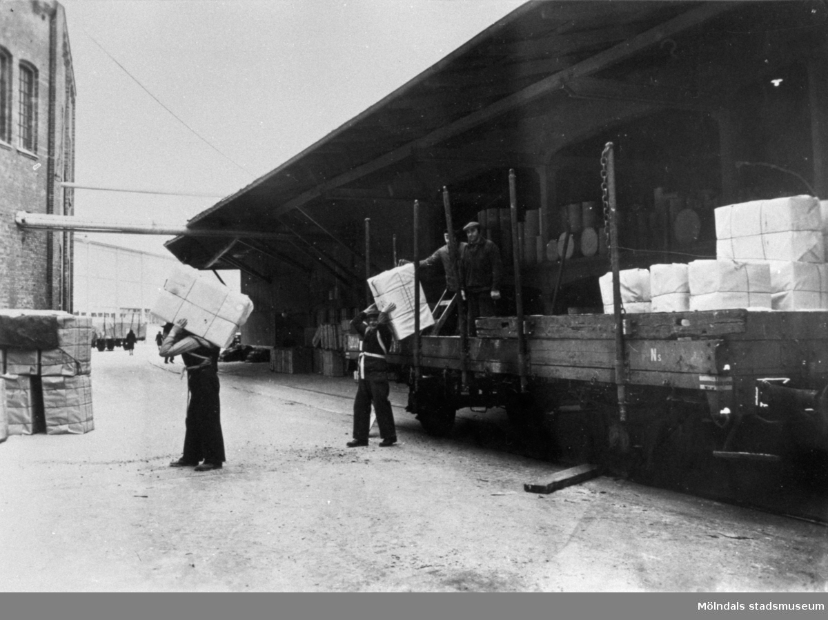 Massabalar lossas på Papyrus i Mölndal. Balarna vägde 200 kg och bars på ryggen. Mannen närmast järnvägsvagnen, som just tar en massabal på ryggen, hette Hjalmar Selander.