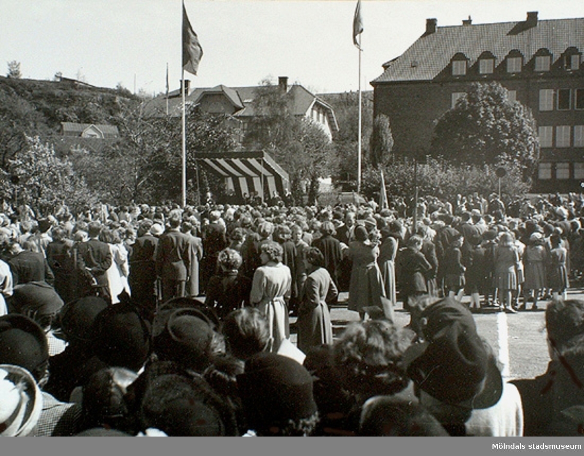 Människor har samlats på Nya torget för att se kung Gustaf VI Adolf vid invigningen av Gunnebo slott den 16 maj 1952 i Mölndals centrum. Till höger ses Kvarnbyskolan.