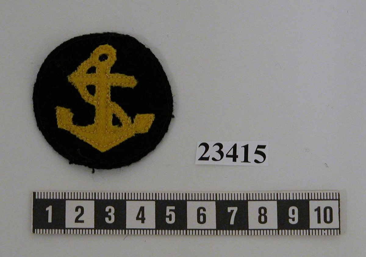 Yrkesbeteckningen för aspiranter vid sjöofficerslinje består av en rund lapp av mörkblått kläde. På lappen sitter ett stockankare med tross sytt i gult kläde.