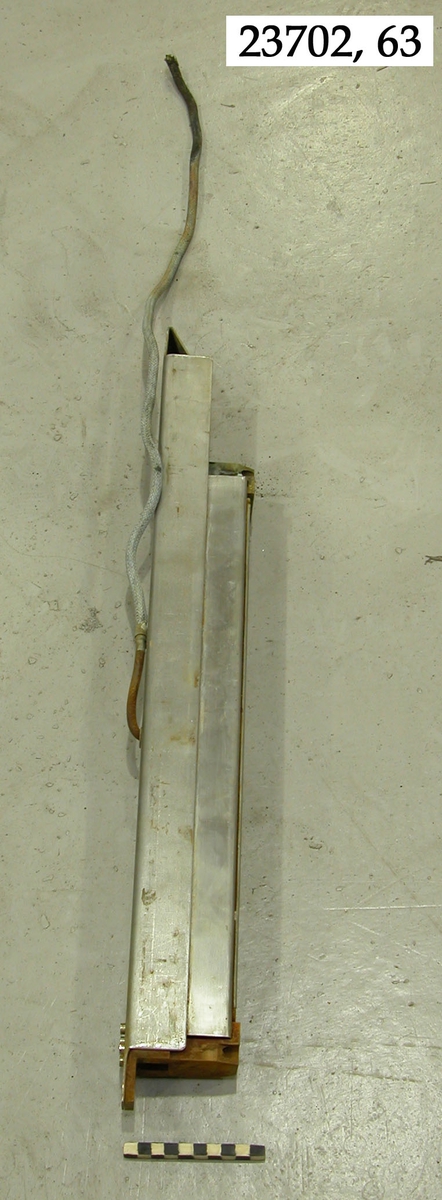Avlång metallren konstruktion. Svängaren består av ett metallhölje och innanför detta sitter en gummidel, med vitfärgat gummi märkt "D". Från svängarens ovansida går en avklippt kabel. I svängarens respektive kortändor sitter monteringshål och påhäktningsanordningar.