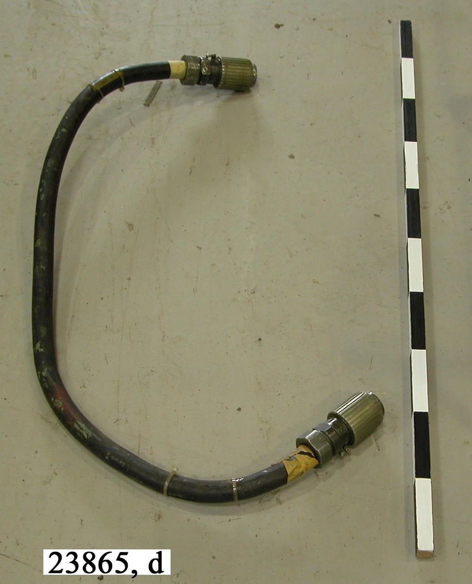 Kabel av gummi. I ändarna sitter grönlackerade kopplingsanordningar av aluminium. Kopplingarna har ytterst gängade hylsor vilka används för att låsa bakeln till instrumentet.