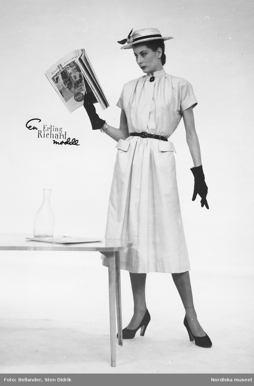 Modell, troligtvis Erika Sundth, i klänning med skärp, stråhatt, pumps och handskar, tidning i handen. Från Erling Richard.