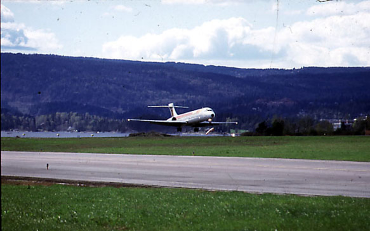 Lufthavn, 1 fly like over bakken, EC-EZA MD-87 fra Iberia. Skrått forfra, - take off. Røykdott bak.