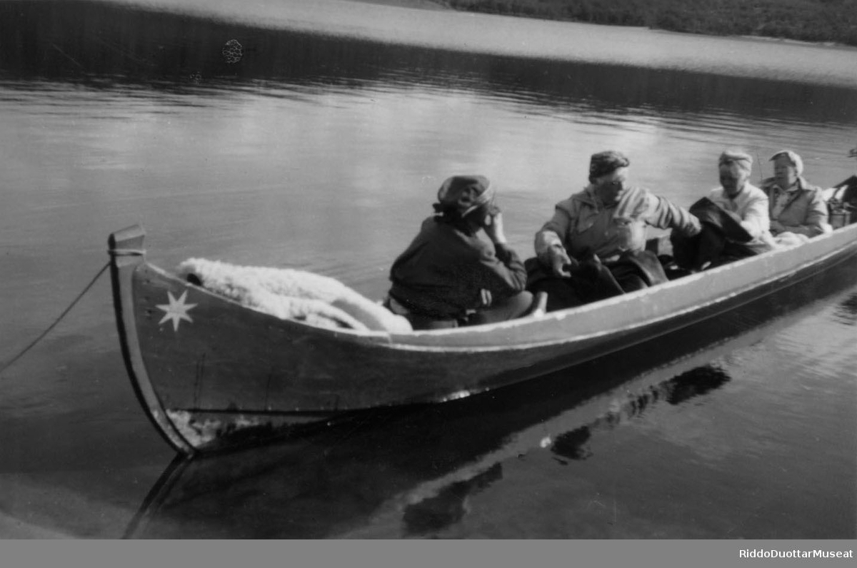 Njeallje olbmo cohkkájit fatnasis.
Fire personer sitter i en elvebåt.