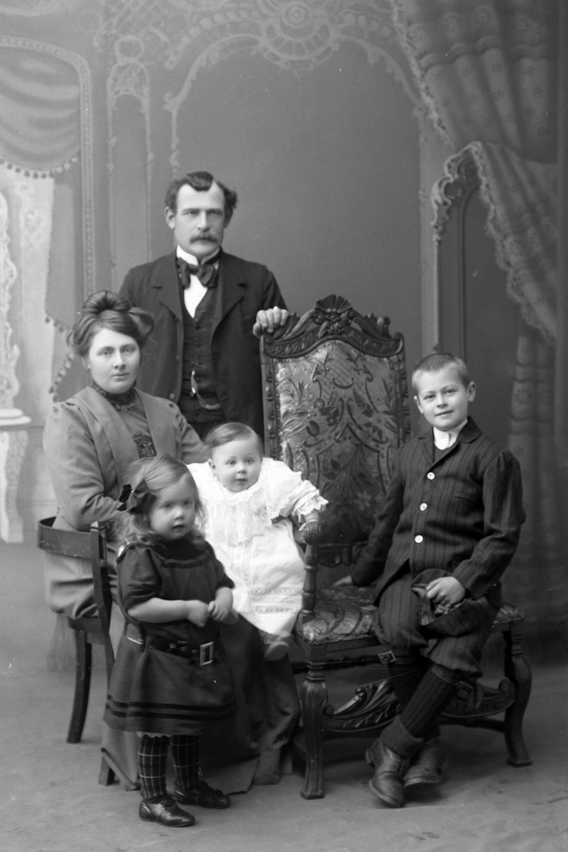 Studioportrett av en familie bestående av mor, far og tre barn.
