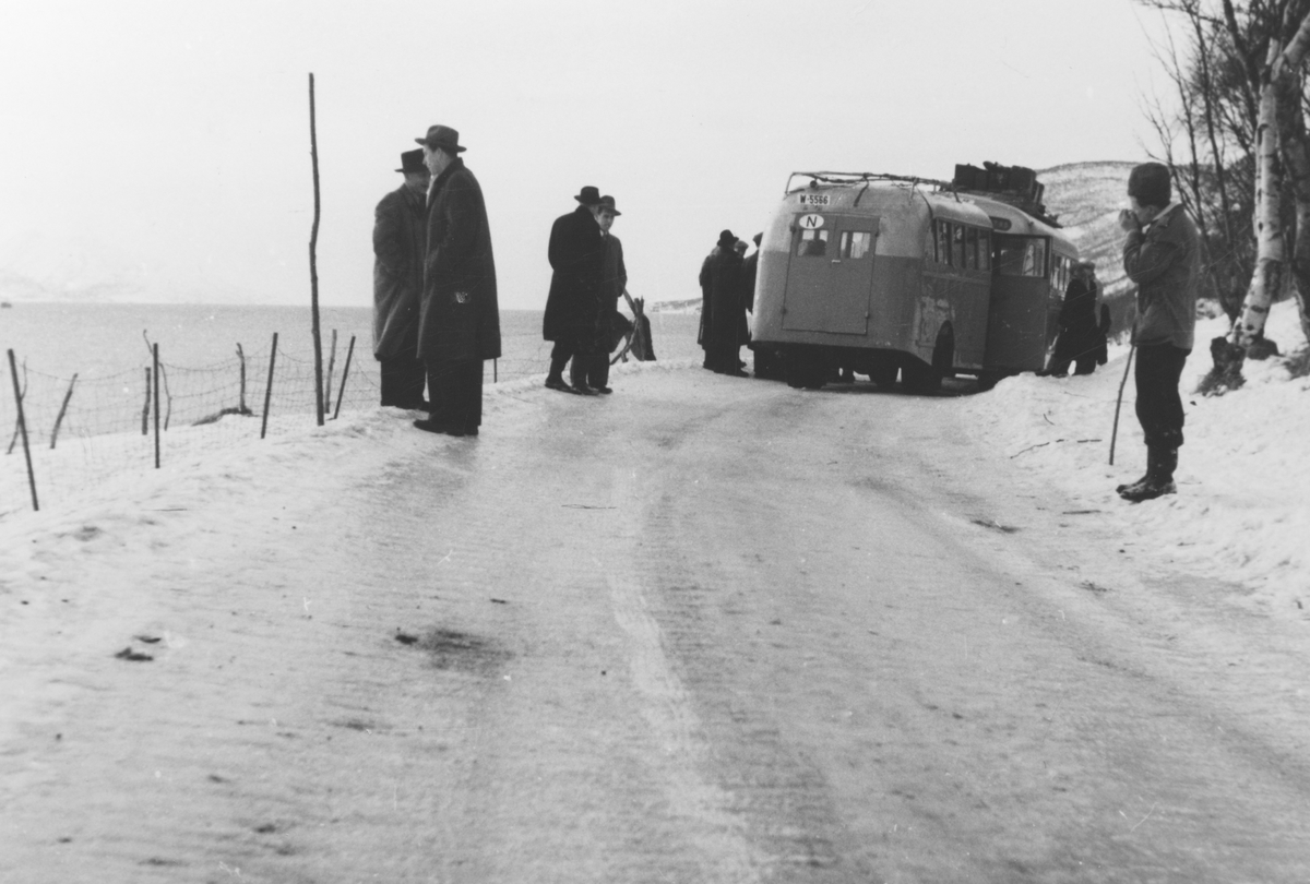 To busser på en vintervei, med passasjerer stående rundt.