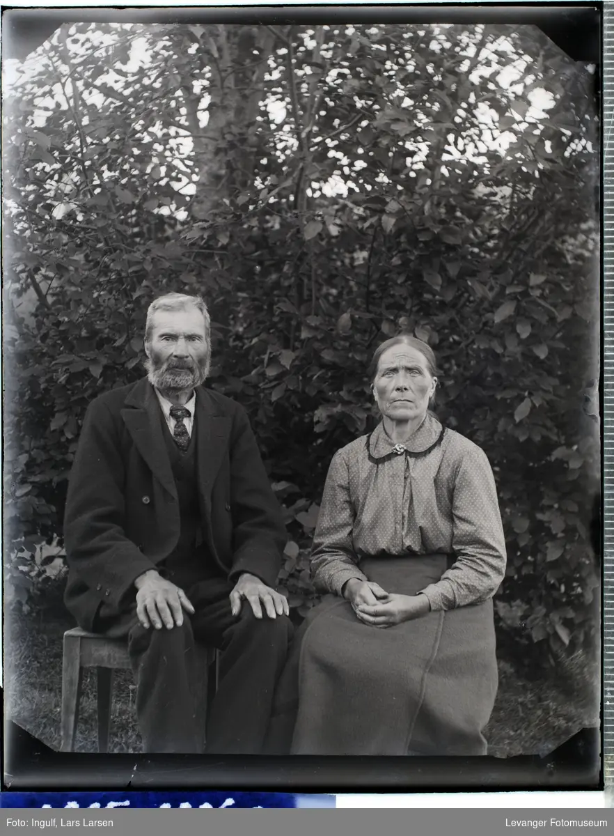 Portrett av eldre mann og kvinne i helfigur i dress og bluse med skjørt.