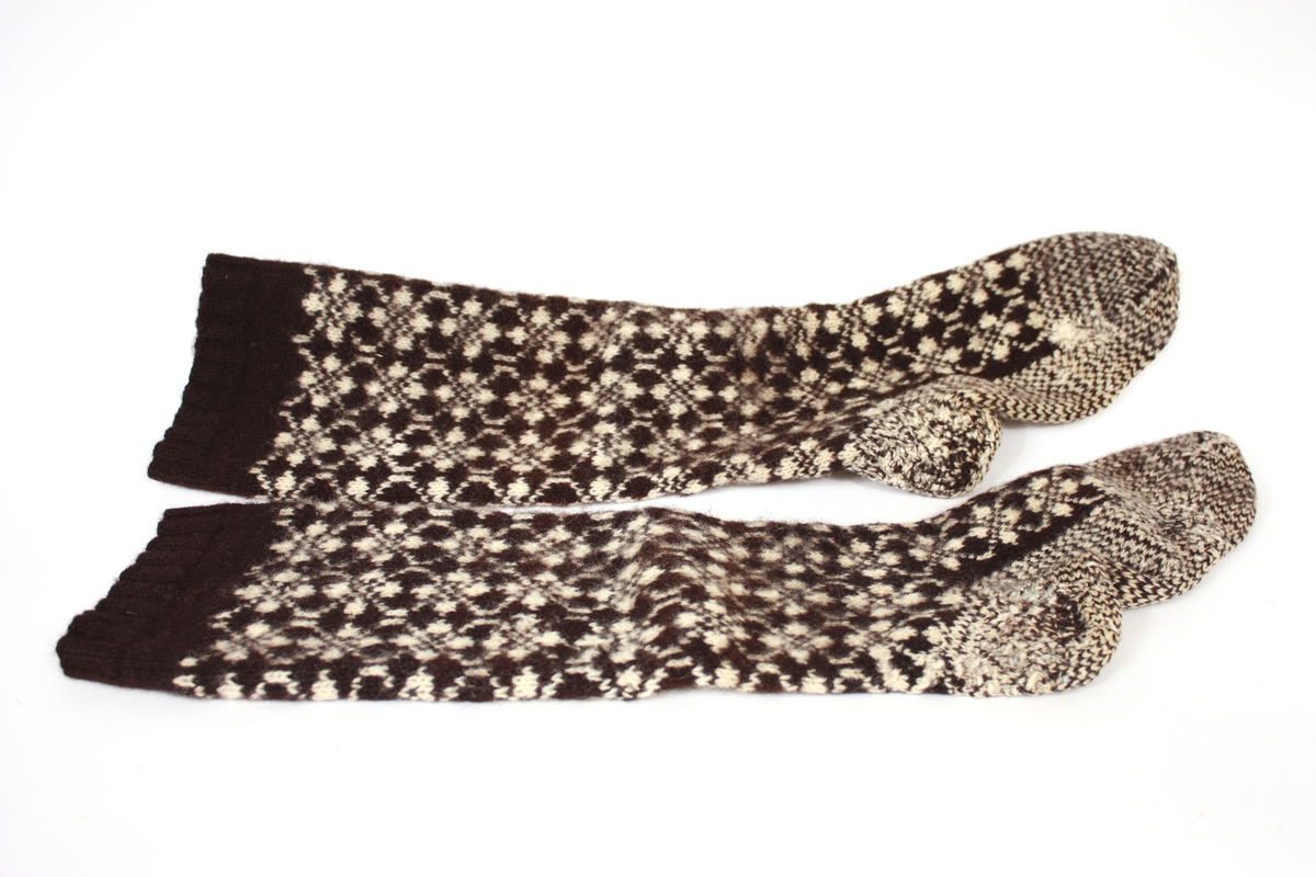 Knelange sokkar med einsfarga brunt felt heilt oppe før det går over i heilmønstra strikk. Hæl og underdel av for er strikka med lus, dvs annakvar mase brun og kvit.
