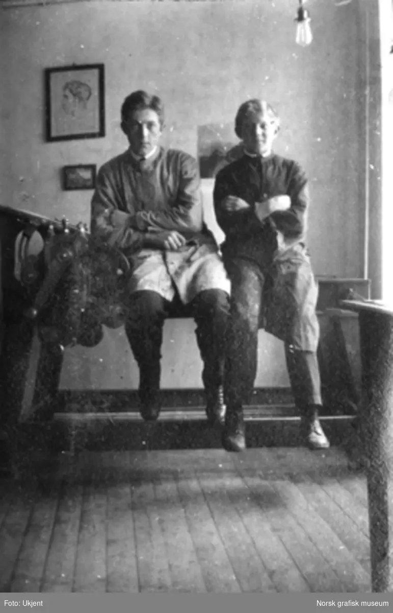 To unge menn sitter på et bord og dingler med bena. På Dreyers Reproduktionsanstalt.

Albumtekst:
"To han(n)er paa Vaglet. T.B.  O.J."