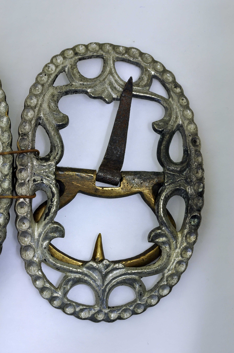 Fra protokoll: 1 par skospænder av fortinnet bronse med gjennembrutt bladverk og rand av hul perlesnor.