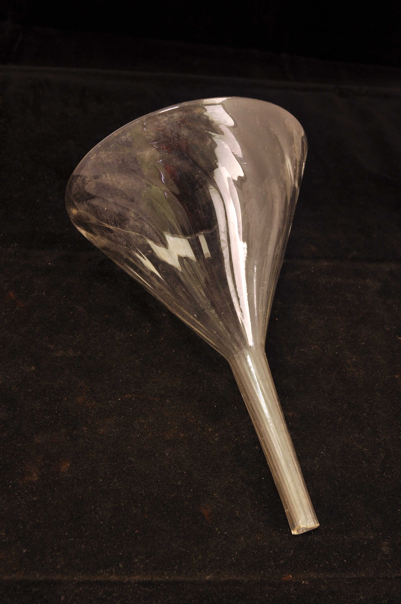 Fra protokoll: Syre-trakt, av glas, med bølgeliner i godset. Diam. = 12,8, l. = 19 cm.