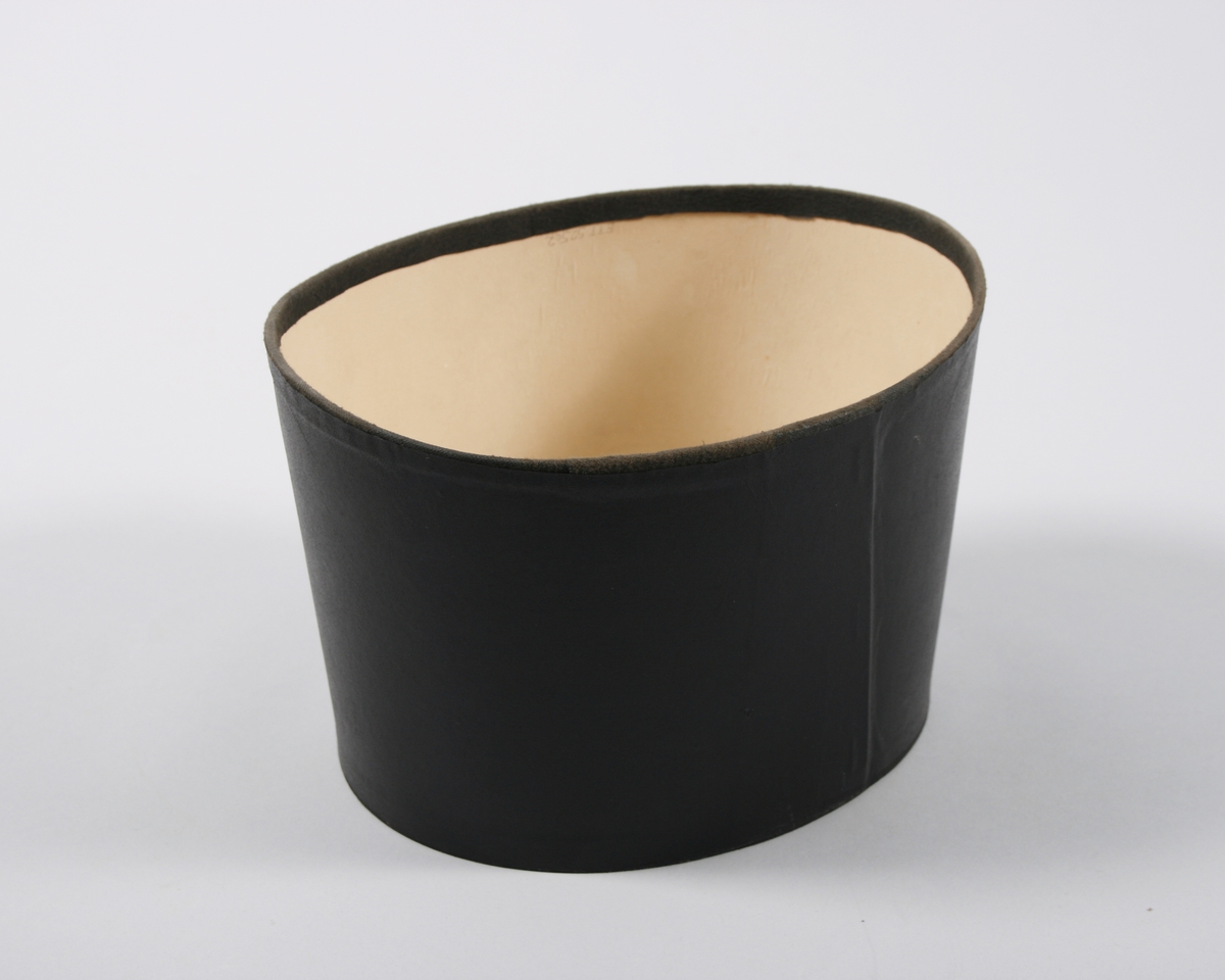 Oval utsillingsboks med pålimt tekstilkant øverst. Esken er stiftet i siden og limt i bunn. Tregt på utsiden med sort papirmateriale.