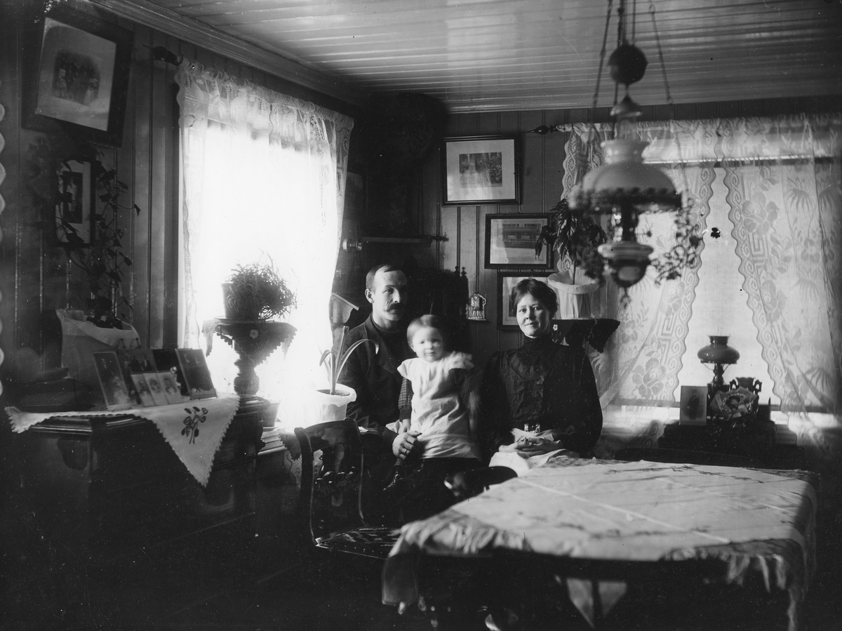Familiebilde. 
På bildet er til venstre Paulmar Sigurd Bolstad og til høyre hans kone Sofie Charlotte Bolstad (født Simensdatter) med barn Else Bolstad (gift Bjerke).
Else ble født 1 februar 1909, hun er mor til informant Pål Bjerke.
Bildet er fra Østhagen.
Stueinteriør.