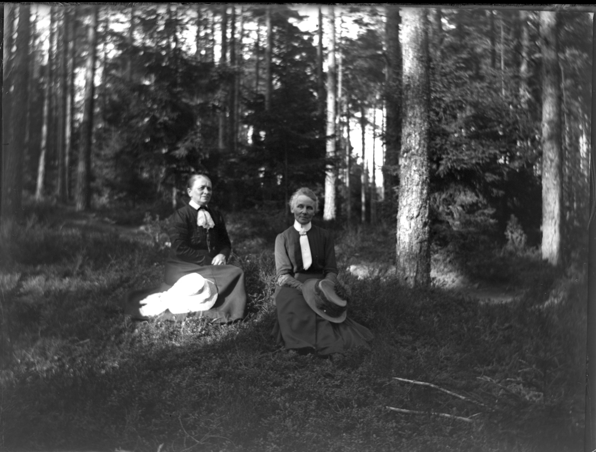 'Bildtext ev: ''Andersson, Lundstron.'' :: 2 kvinnor sittande på marken, tallvegetation i bakgrunden. ::  :: Ingår i serie med fotonr. 5229:1-13.'