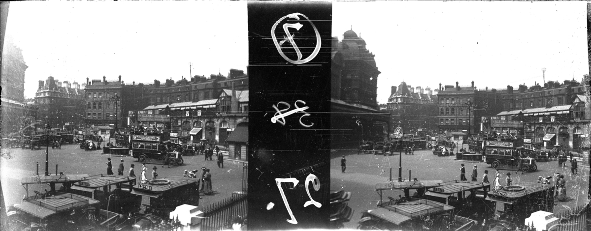 'Bildtext: ''Victoria station yard (Sunday).'' :: Gatuvy med bussar, människor och hus. Gatlykta. ::  :: Ingår i serie med fotonr. 5263:1-16. Se även hela serien med fotonr. 5237-5267.'