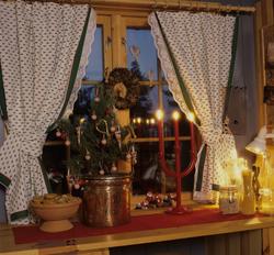 Et julepyntet vindu med gardiner, lys, kaker og et lite jule