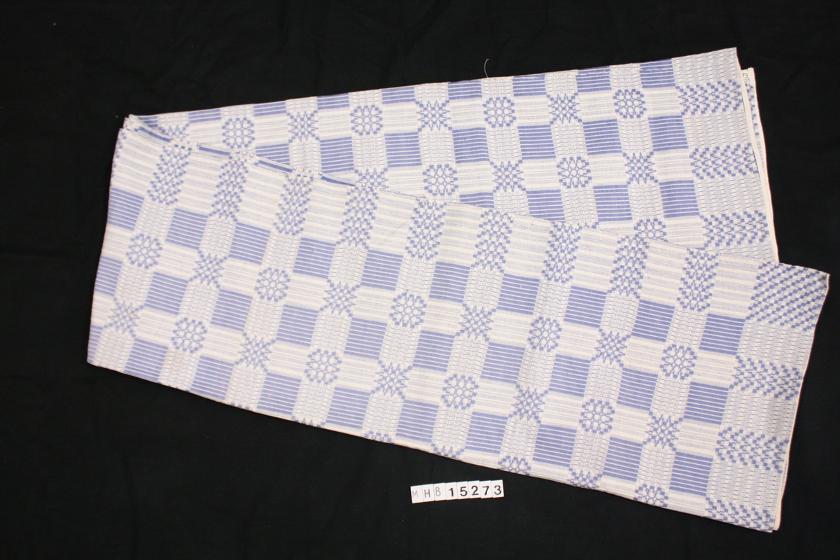 Trolig en duk. Mønstervevet  tekstil, rektangulært, kortsidene er sydd inn med slitebånd. Langsidene er jarekant.