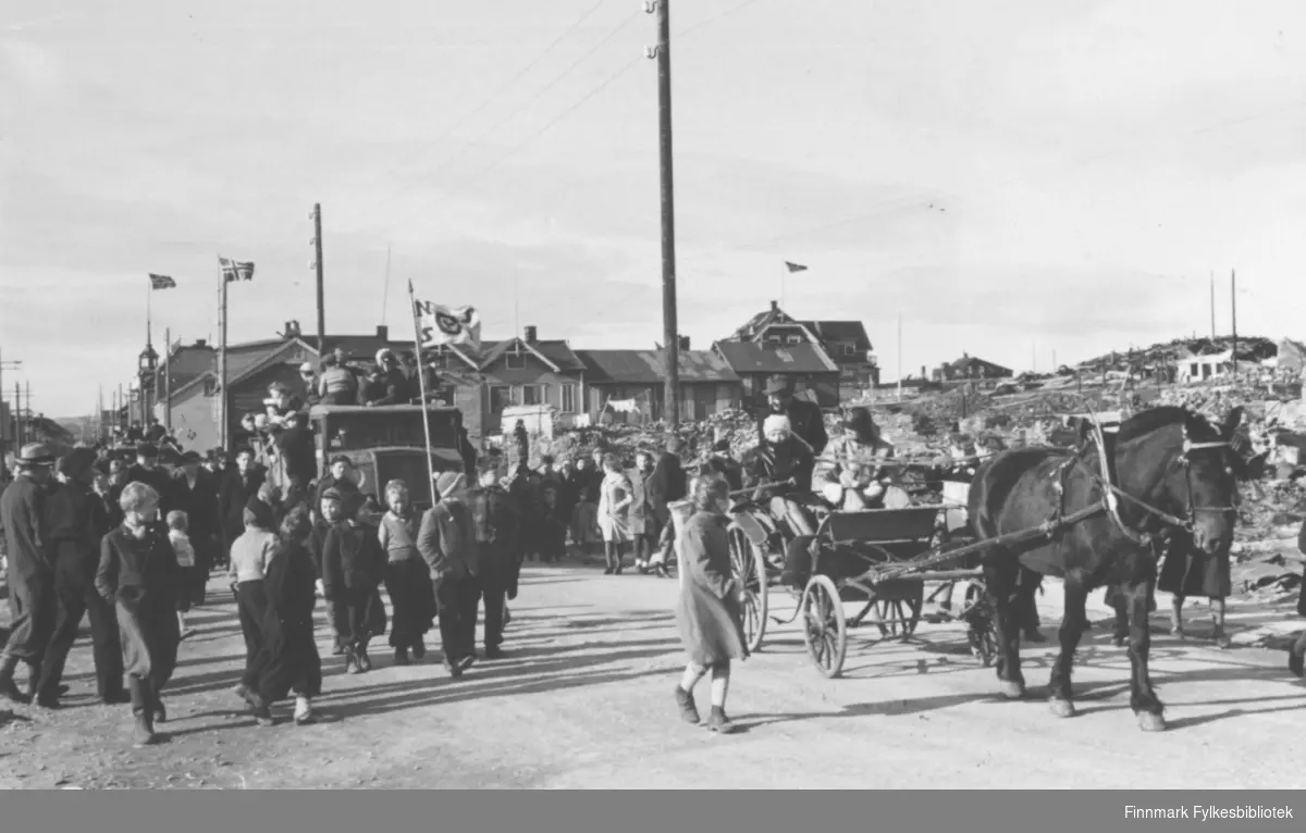 'Gatebilde fra Vardø 1945.' Et opptog gjennom gatene. Flere barn. En hest med vogn.