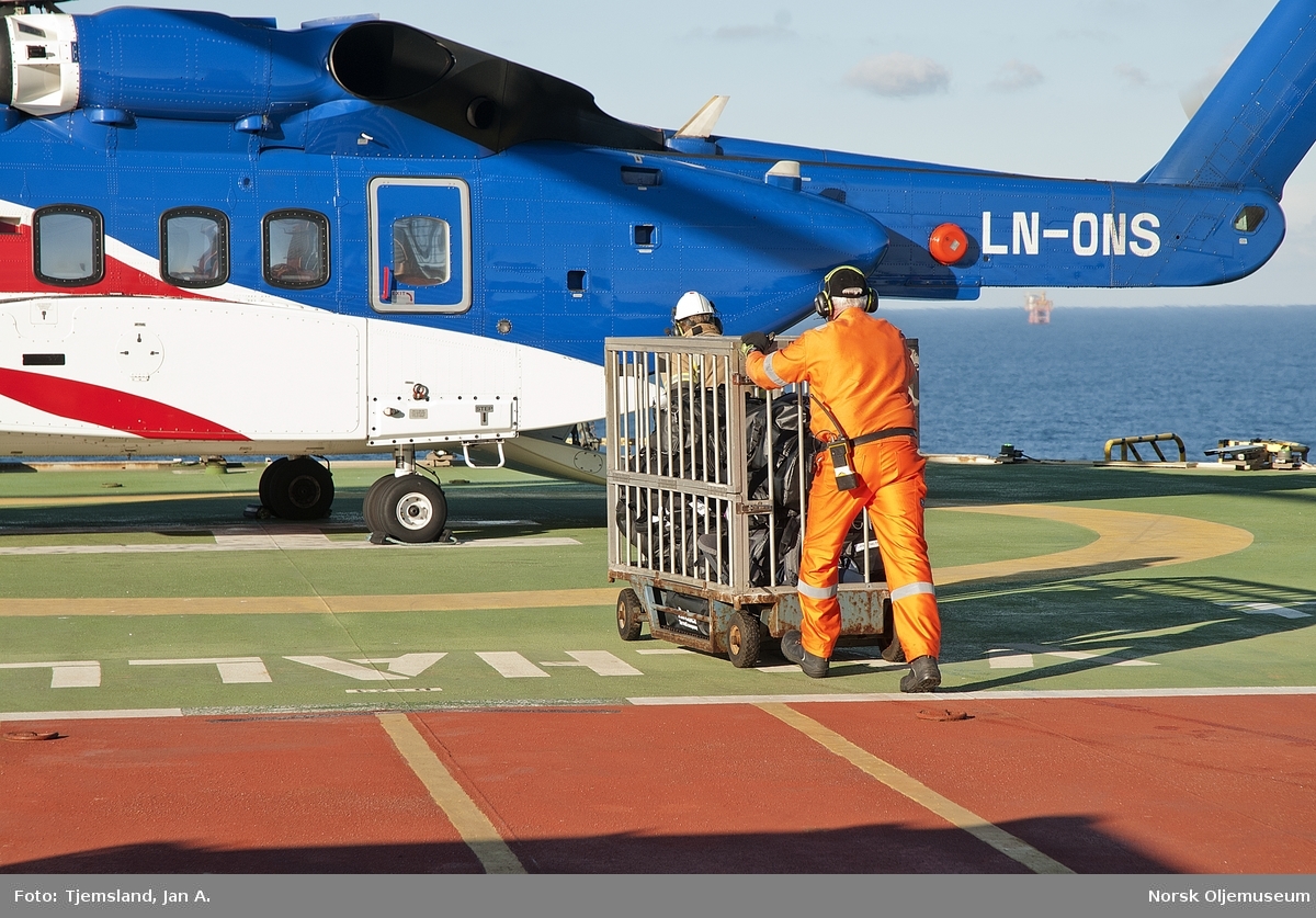 HLO personell sørger for at passasjerenes bagasje kommer ut til helikopteret før det igjen setter kursen mot fastlandet.
Harry Bushmann i orange kjeledress går bakerst og dytter trallen.