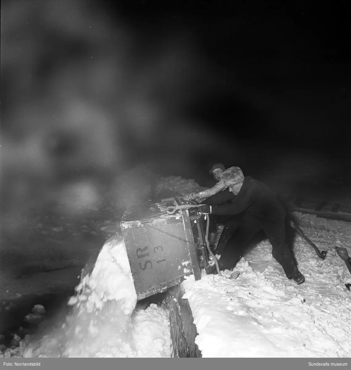 Efter ett rejält snöfall i december 1949 var det full huggning för stadens snöröjare. Elva mil gator och vägar skulle röjas och sandas, själva plogningen sköttes maskinellt men när det sedan var dags för bortforsling av snöhögar och vallar kom de fyrfota trotjänarna fortfarande till sin rätt.  Här är det Axel Svensson som styr Diana nedför Esplanaden för att tippa ännu ett snölass i Selångersån. Renhållningsverket hade 60 man i personalstyrkan vid den här tiden och hade tillgång till 15 lastbilar, varav tre moderna framhjulsdrivna som var mycket användbara i den backiga terrängen, elva snöplogar och två traktorer med snöskopa. Och så de åtta hästarna förstås. Vid katastroftillbud med osedvanlig halka eller hård snöstorm kunde man dessutom ta in 20-30 extra hästar och 20-100 extra arbetare. Den här vintern såg verkets chef, A.S. Nilsson, mycket fram emot en nymodighet på ingång till maskinparken, nämligen snöslungan. Bakom hästekipaget på en av bilderna syns den numera rivna biografen Röda Kvarn.
