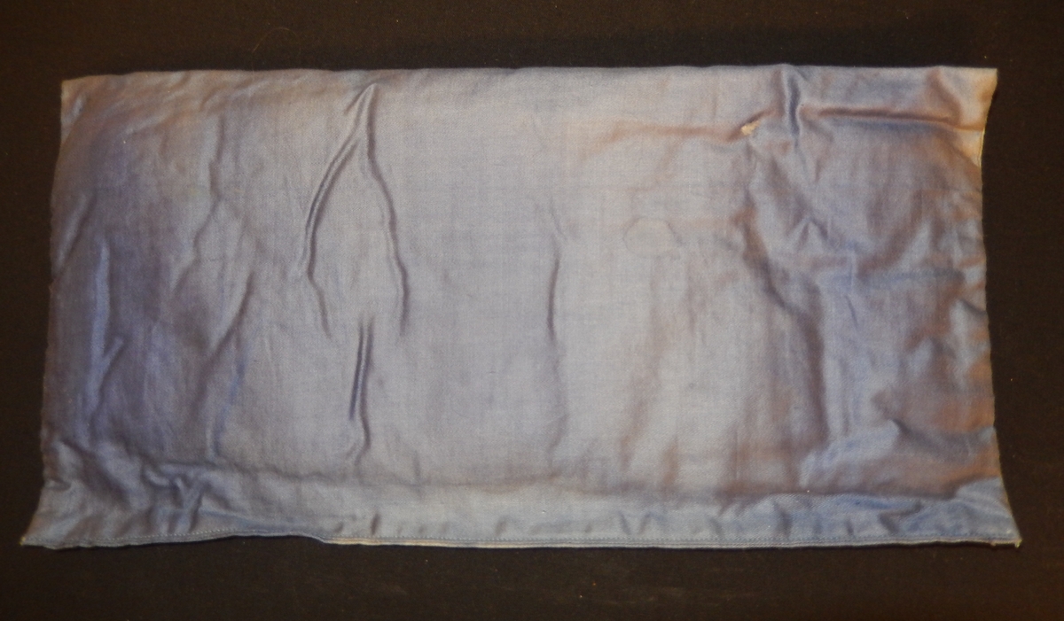 En dokkeseng i kurvfletting fra ca. 1905, med løse sengegavler, en madrass, et laken (glasshånklr med monogram), en overmadrass, to puter, med putevar, en dyne og et heklet sengeteppe.