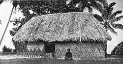 Person sittende utenfor et stort hus laget av strå på Tonga