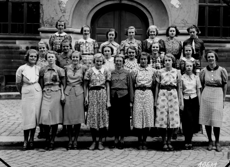 Olaus Petriskolan, 21 skolflickor med lärarinna.
Skolbyggnad i bakgrunden.