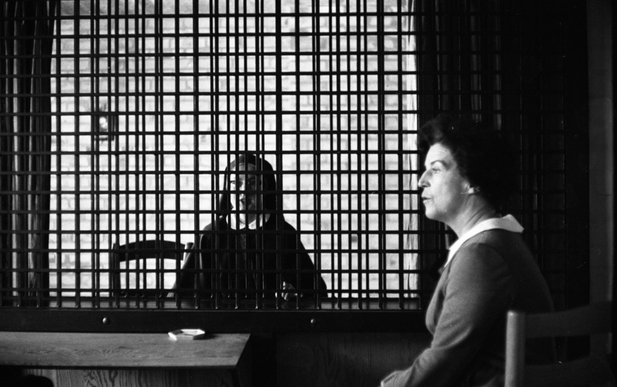 Länstös blev nunna 14 november 1966

Närbild på en ung nunna klädd i dok och dräkt. Hon bär glasögon och sitter bakom galler i bakgrunden. Framför gallret sitter en äldre kvinna klädd i en tröja med vit krage.