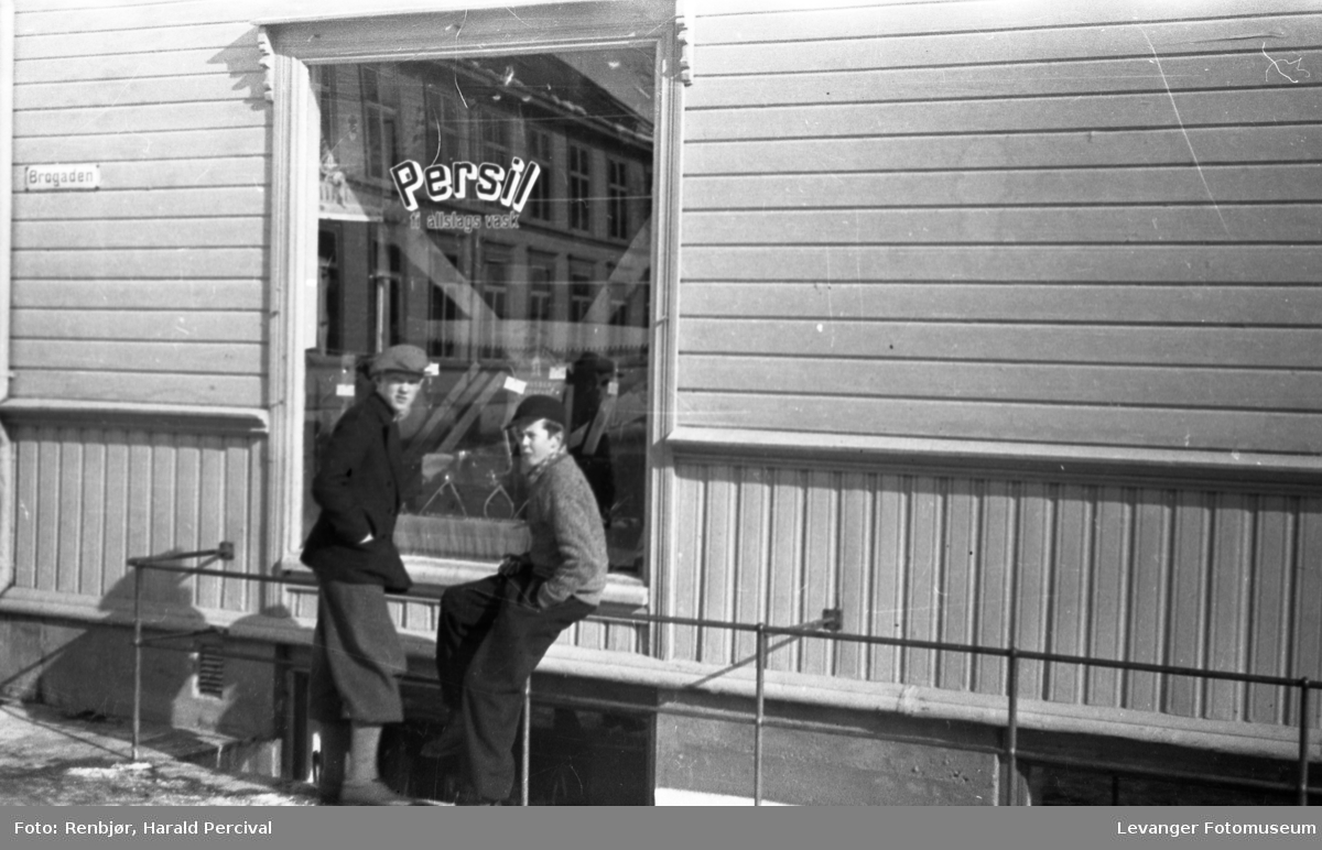 To gutter foran en butikk med reklame for Persil på vinduet.
