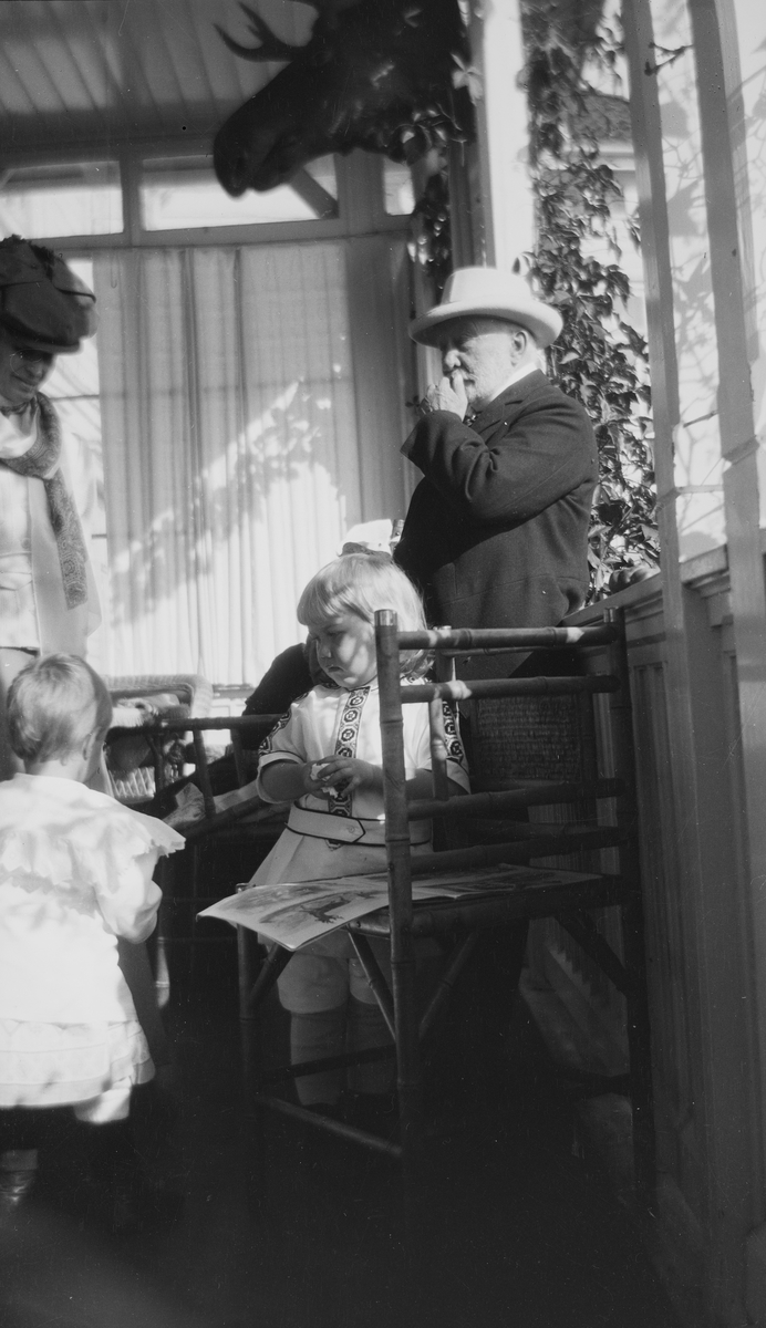 En uidentifisert kvinne og Haaken Christian Mathiesen står sammen med et uidentifisert barn og Iacob Ihlen Mathiesen på en veranda.