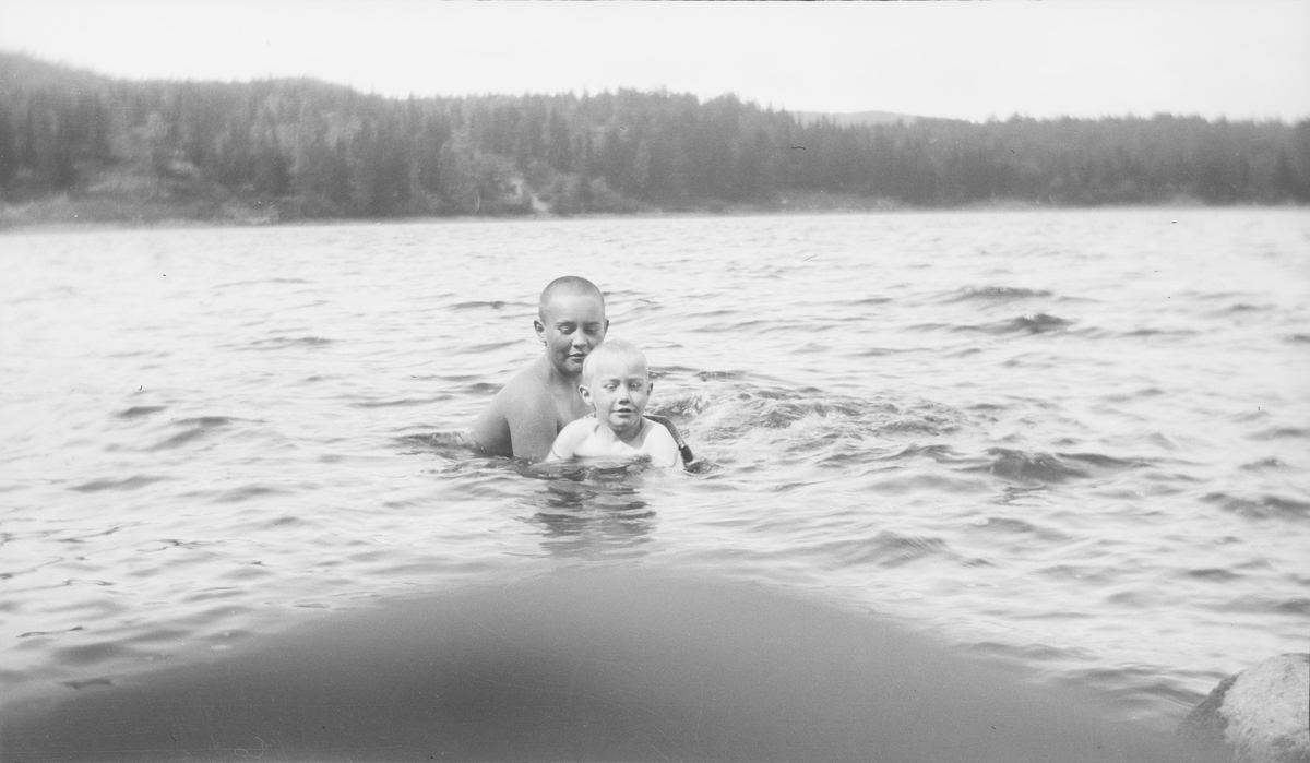 En eldre gutt hjelper en yngre gutt (trolig Iacob Ihlen Mathiesen) med svømmetrening i en innsjø på østlandet. Den yngste gutten har på svømmebelte.